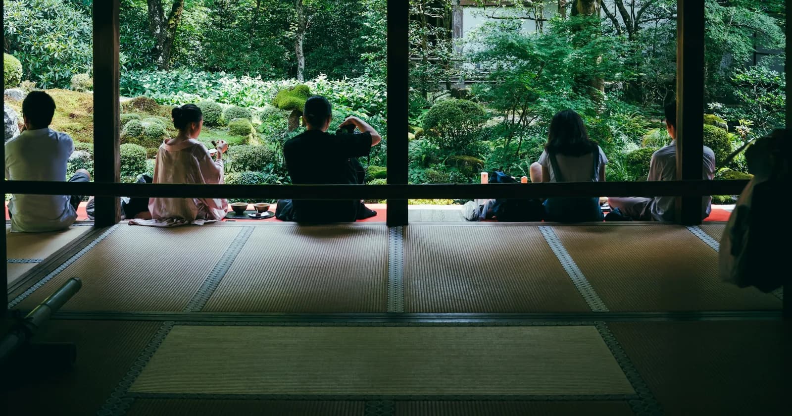 寺院の縁側に並んで庭を眺めながら抹茶をいただく人たち